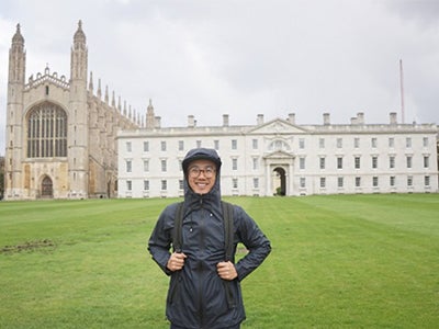 Stern MBA student Dennis Au, wearing rain gear, stands in front of a building on the campus of the London Business School.