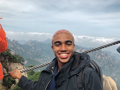 Business student Dimitri Pun holds a rope fence while smiling in front of a scenic view during his study abroad trip to Shanghai. 