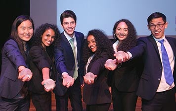 The six students who won the ISP Competition hold out their globe-shaped trophies on the Skirball stage.