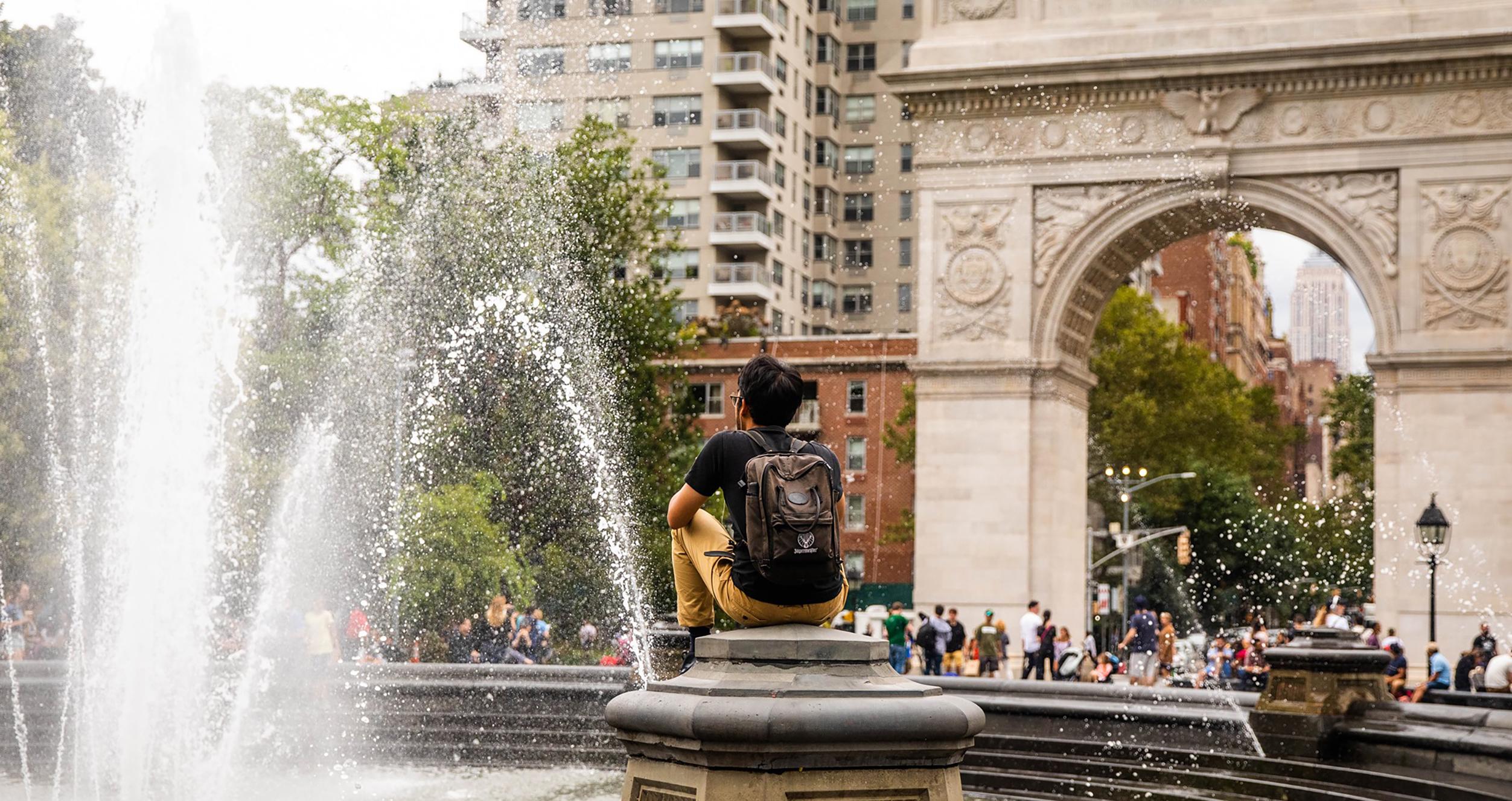 Student sitting near fountain in front of Washington Square Arch