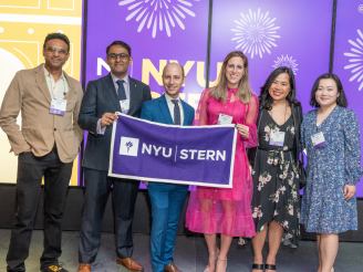 Six alumni pose with an NYU Stern banner at the Reunion 2023 celebration at MoMA.