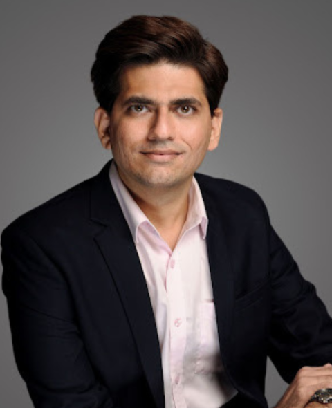 Nilesh's headshot. He stares at the camera with brown hair and a black suit jacket.