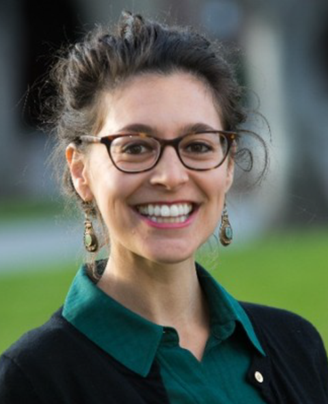 A portrait of Allyson Dhindsa - A brown haired white woman, smiling at the camera in a green collared shirt