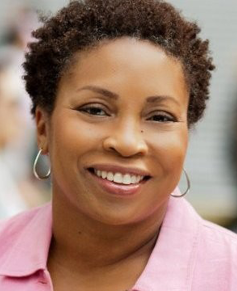 A portrait of Kim Lewis-Collins - A Black woman in a pink shirt smiling at the camera