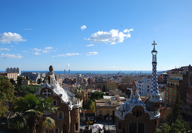 A view from the hillside of Gaudi's Park Guell in Barcelona shows the city against a vivid blue sky.
