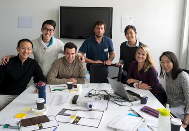 MBA student Cara Witt-Landefeld works on a group project with other students while gathered around a conference table littered with coffee cups and papers.