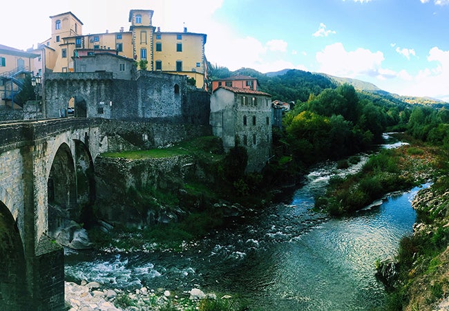 Water flows under a stone bridge on a bright, sunny day in the city of Pisa.