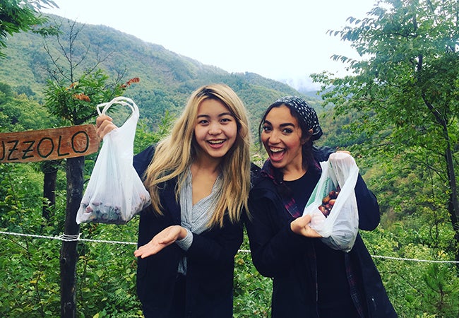 Undergraduate student Alexandra Grieco and a friend hold up clear bags filled with chestnuts in a forest setting.