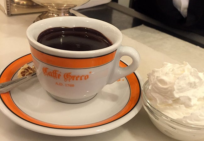 Very thick, dark hot chocolate is served in a cup that says "Café Greco" in orange lettering. 