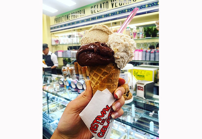 A woman holds a waffle cone with three scoops of dairy-free gelato piled on top. 