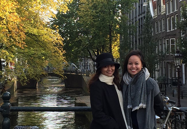 MBA student Kimberly Rodriguez stands with a friend on a bridge next to a canal in the fall. 