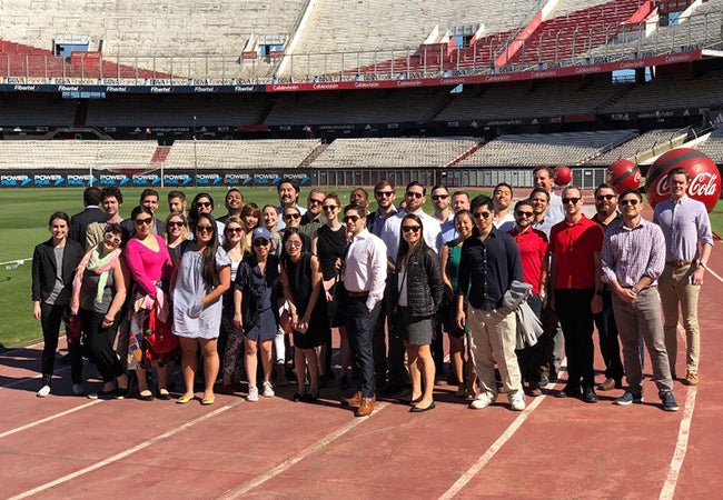 A group of MBA students in Argentina pose inside of a large empty stadium. 