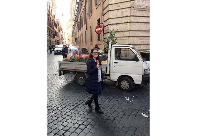 MBA student Ashley Grand walks down a stone street holding a cone of red gelato while studying abroad in Italy.