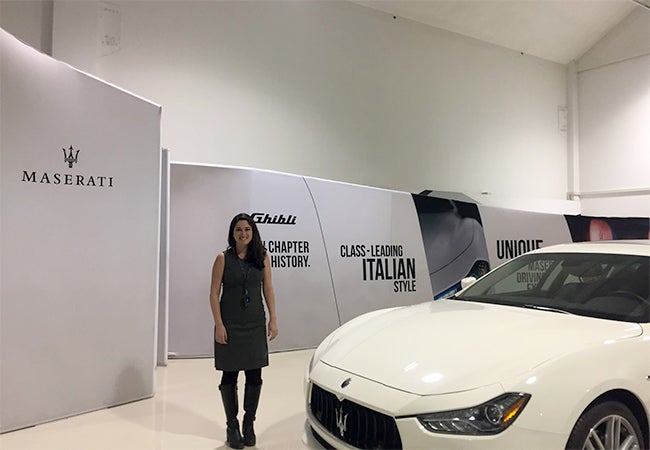 MBA student Ashley Grand stands next to a white Maserati car while visiting the Italian automaker's facilities. 