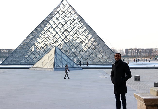 MBA student Calvin Mack stands outside and in front of the Louvre's iconic glass triangle ceiling.