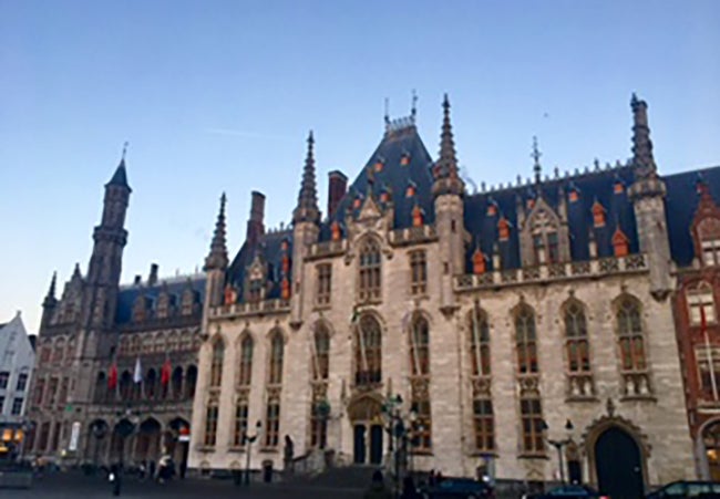 A stone building in Bruges, Belgium with many narrow turrets on a clear day.  