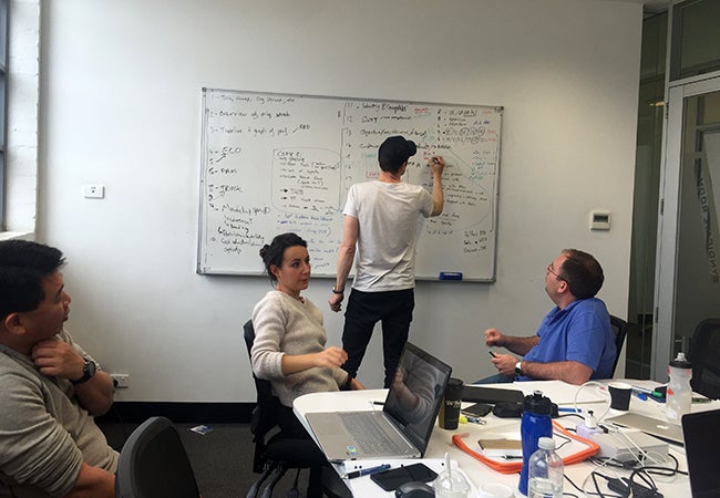 One student writes on a whiteboard while three others discuss their strategy during a group work session at Melbourne Business School.