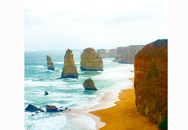 Gentle waves from the sea swish around orange cliffs and rock formations in Australia. 