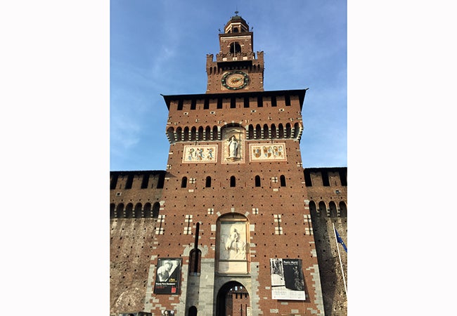 A beautiful clock ticks away time on the brown decorative facade of Castello Sforzesco.