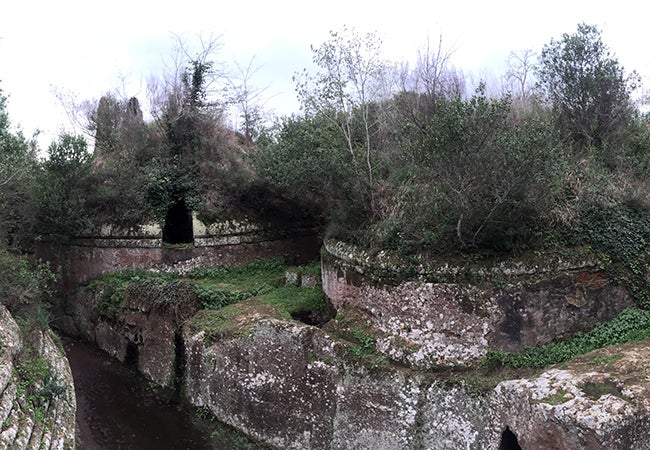 Grass and other foilage partially obscures circular stone tombs at the Etruscan Necropolises of Cerveteri and Tarquinia.