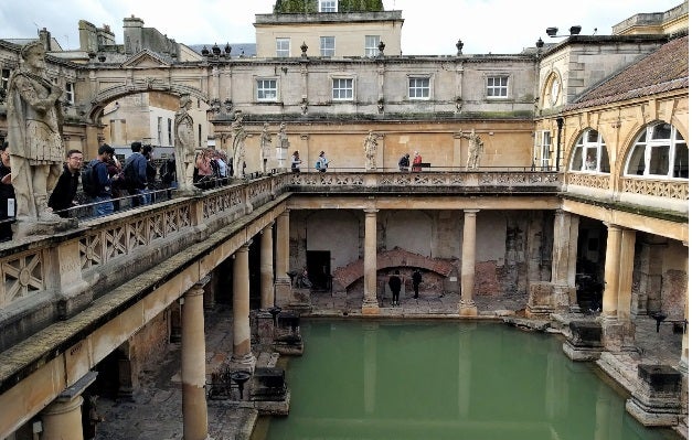 Visitors gaze down over a stone railing at ancient roman baths in the town of Bath, England. 