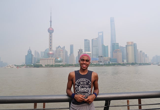 Undergraduate business student Dimitri Pun stands in front of a river with the Shanghai skyline in the background. 