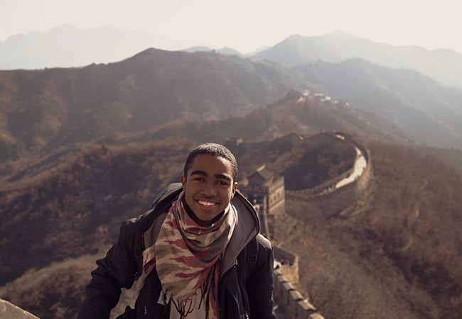 Business student Dimitri Pun smiles at the camera while walking the Great Wall of China. 