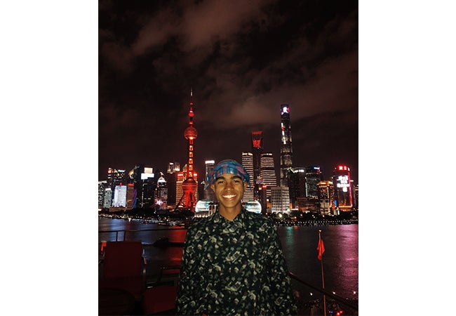 Undergraduate business student Dimitri Pun stands in front of a Shanghai city scene at night. 