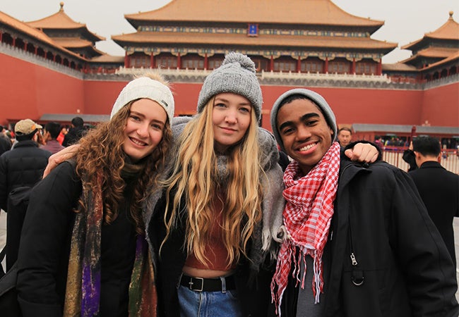 Undergraduate business student Dimitri Pun links arms with friends in front of a red building while studying abroad in Shanghai. 