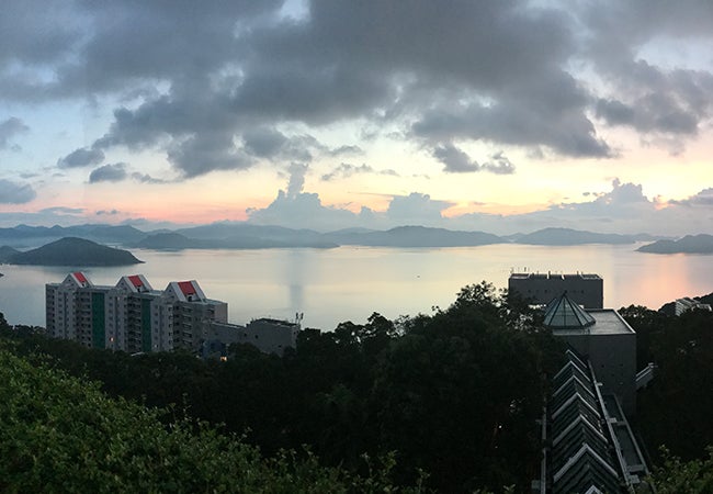 The sun sets over a lake in Hong Kong with a line of multi-story buildings on the shore below. 