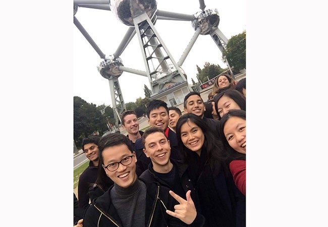 A group of students gather for a photo together in front of a large metal structure in Brussels. 