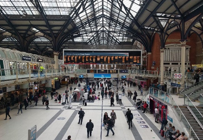 Pedestrians stream through a busy station with a glass roof in the London underground transit system.