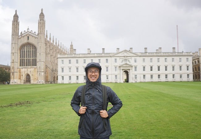 Stern MBA student Dennis Au, wearing rain gear, stands before a building on the campus of the London Business School while studying abroad.