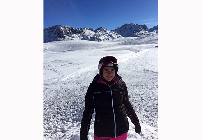 MBA student Ashley Grand, dressed in ski goggles and gear, stands before a snowy mountain region of the Italian Alps.