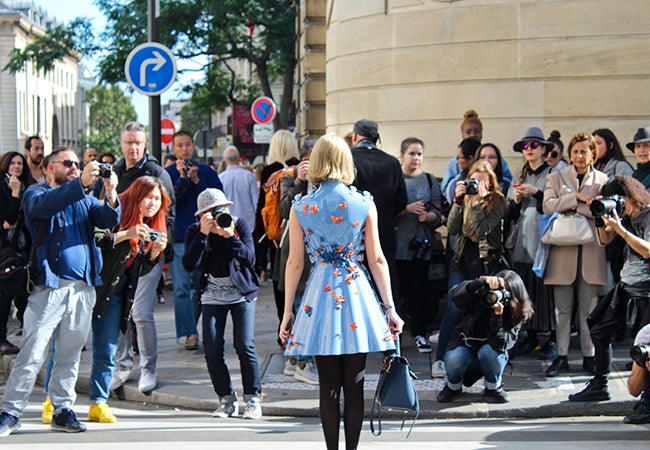 Undergraduate student Michelle Enkerlin wears a blue dress in front of photographers on a city street.