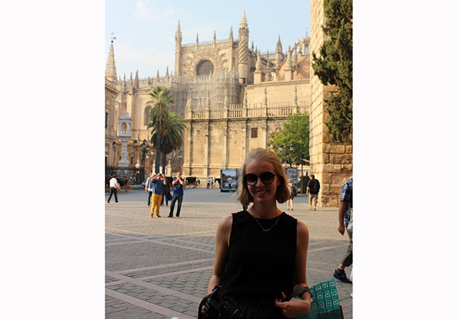 Undergraduate student Michelle Enkerlin stands before a tall and magnificent building in a stone city square.