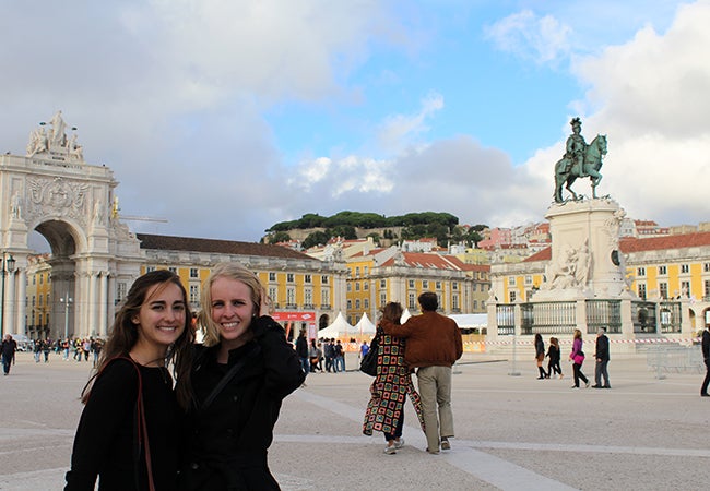 Undergraduate student Michelle Enkerlin stands with a friend near a statue of a man on a horse in a city square. 