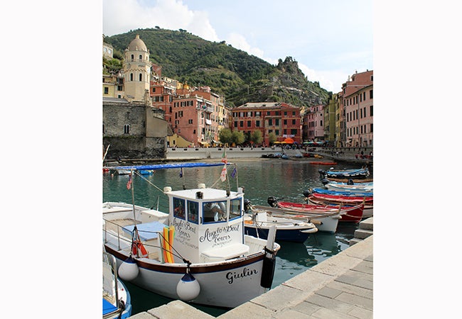 A collection of small boats sit in a calm body of water in a European city. 