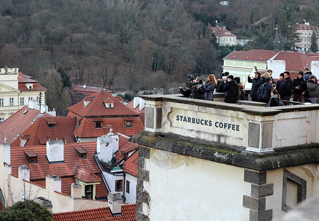 Tourists hold cameras on the roof of a Starbucks that looks out over the John Lennon Wall in Prague.