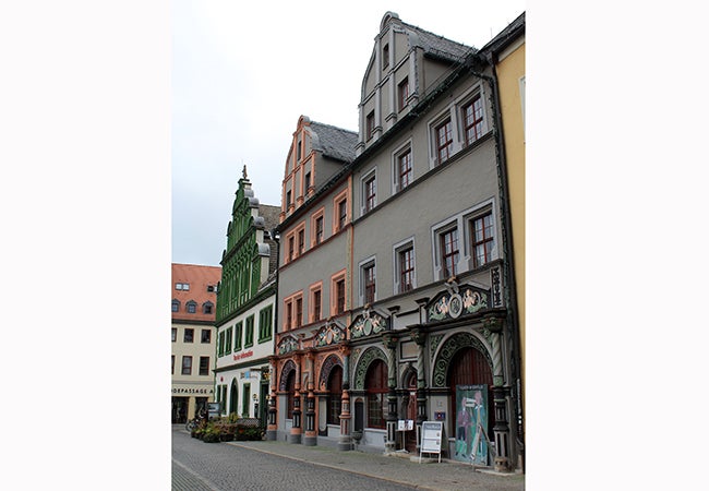 A row of gray and white buildings with colorful accents stands on a stone street in Germany. 