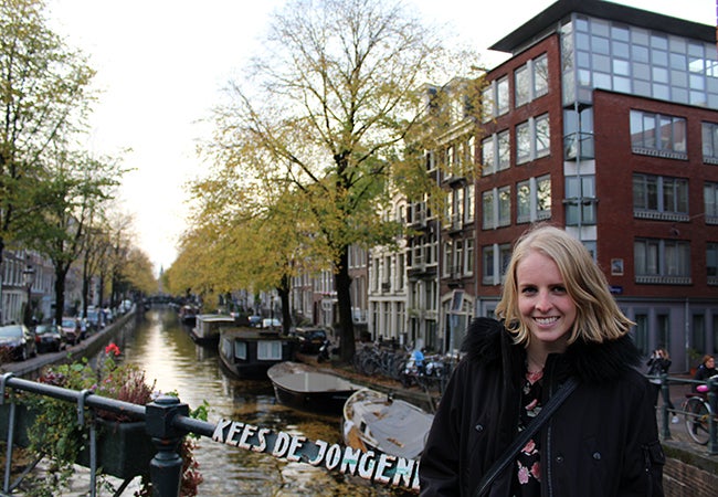 Undergraduate business student Michelle Enkerlin stands in front of a canal in Amsterdam lined with empty boats hitched to one side.