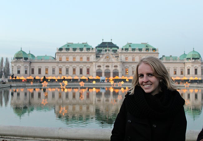 Undergraduate business student Michelle Enkerlin stands before an ornate white stone building with a green roof in Vienna, Austria.