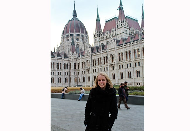 Undergraduate business student Michelle Enkerlin stands in front of a large stone building with red turrets and a red dome.