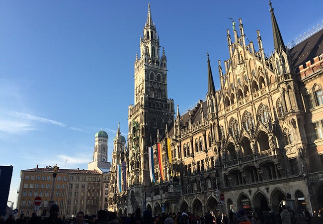 Flags drape across the front of a grandiose stone building in Munich.