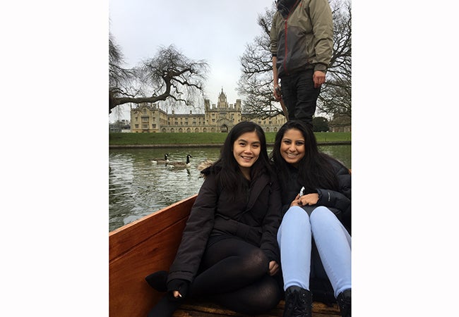 Business student Natasha Lim poses with a friend on a boat in front of a massive stone building in Cambridge. 