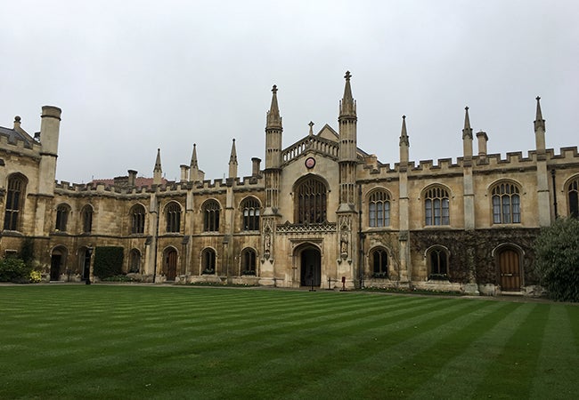 A very old stone building on the Cambridge campus sits on a perfectly manicured lawn. 