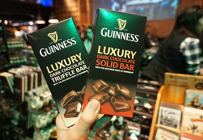 A hand holds up two Guiness dark chocolate bars encased in green packaging. 