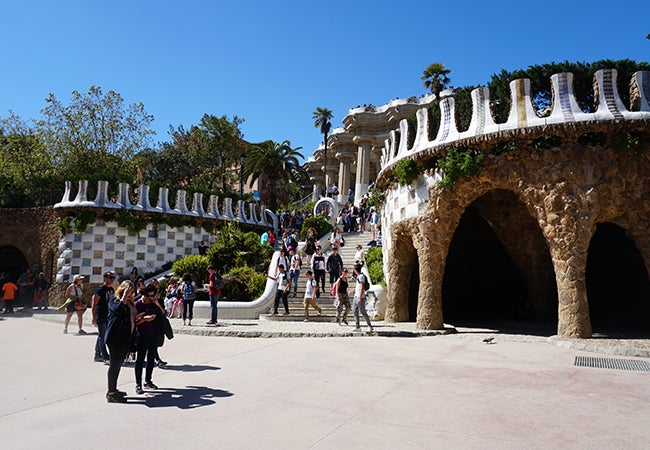 Visitors descend a sunny staircase lined with colorful tiles at Park Güell in Barcelona.