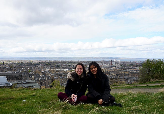 Business students sit in a grassy field in Scotland that overlooks the city of Edinburgh during a study abroad trip. 