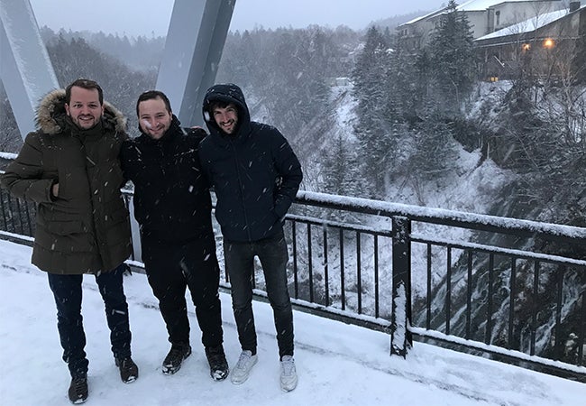 MBA student Ryan and two friends, dressed in parkas, stand outside in the snow in a mountain setting. 